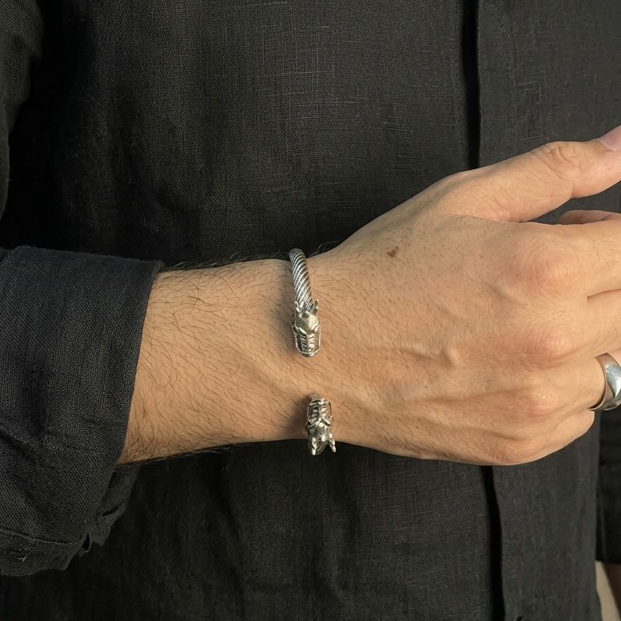 Person wearing two silver bracelets with dragon designs on a black background