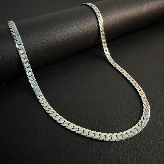 A silver-toned Cuban link chain necklace draped over a black textured cylindrical surface on a dark black background.
