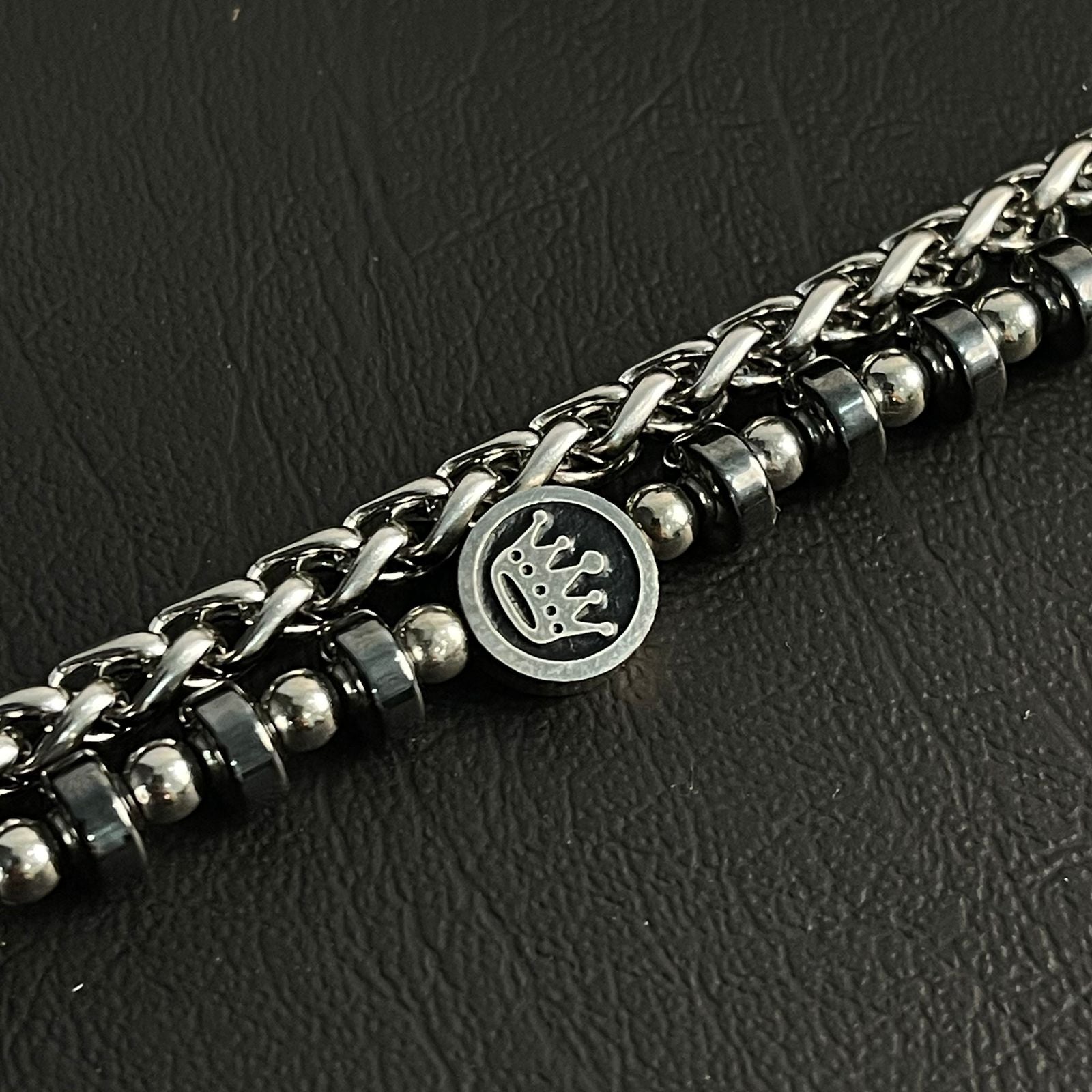 Silver chain bracelet with a crown emblem on a dark textured background